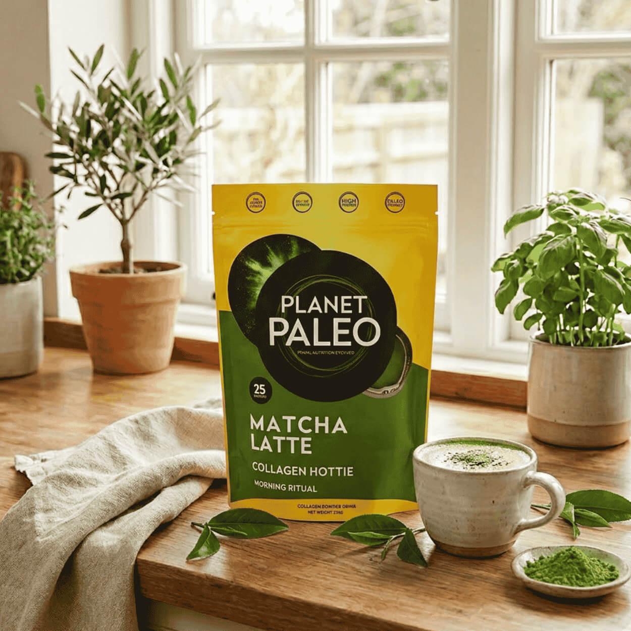 Balení Planet Paleo Matcha Latté vedle šálku zeleného matcha nápoje, metličky a práškového čaje matcha.